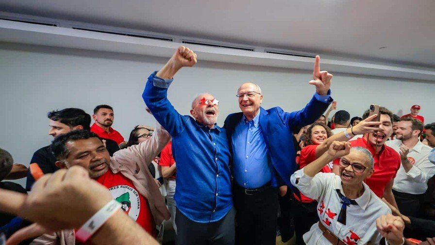 Lula da Silva levanta el puño junto a Geraldo Alckmin, rodeados de seguidores con camisetas rojas en un salón