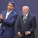 Flávio Bolsonaro, de traje azul, gesticula junto a Luiz Inácio Lula da Silva, sonriente y con corbata verde y amarilla, en un plató de televisión