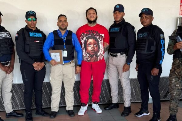 Jhovanny de Jesús Metz Cruz, de camiseta y pantalón rojos, custodiado por agentes de Interpol, la DICRIM, un representante del Ministerio Público y un militar