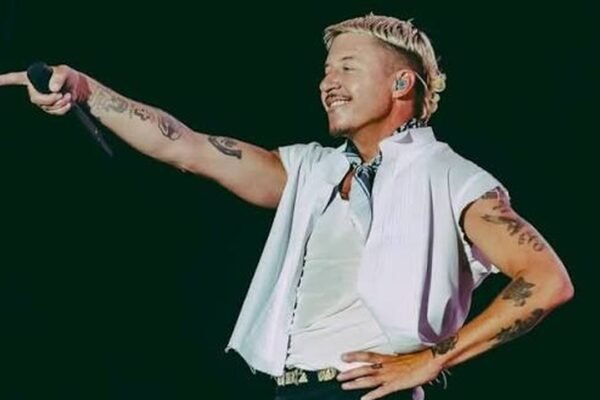 El rapero Macklemore, con camisa blanca sin mangas, señala al público con el micrófono en la mano durante un concierto