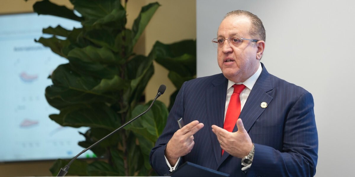 Magín Díaz habla desde un atril con micrófono, con una pantalla y una planta al fondo
