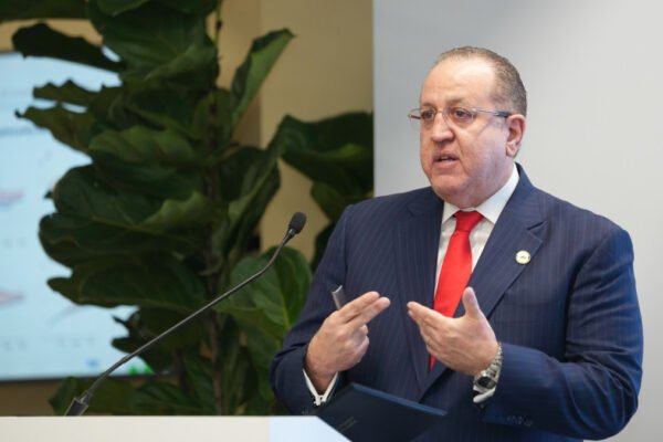 Magín Díaz habla desde un atril con micrófono, con una pantalla y una planta al fondo