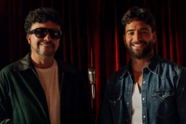 Andrés Cepeda, con gafas oscuras, y Maluma, con camisa de mezclilla, sonríen frente a un micrófono antiguo y una cortina roja