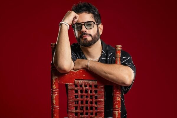 Manny Cruz, con gafas y barba, posa apoyado en el respaldo de una silla roja ante un fondo rojo