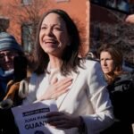 María Corina Machado sonríe con la mano en el pecho rodeada de personas que la graban con sus teléfonos al aire libre.