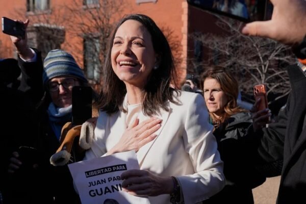 María Corina Machado sonríe con la mano en el pecho rodeada de personas que la graban con sus teléfonos al aire libre.