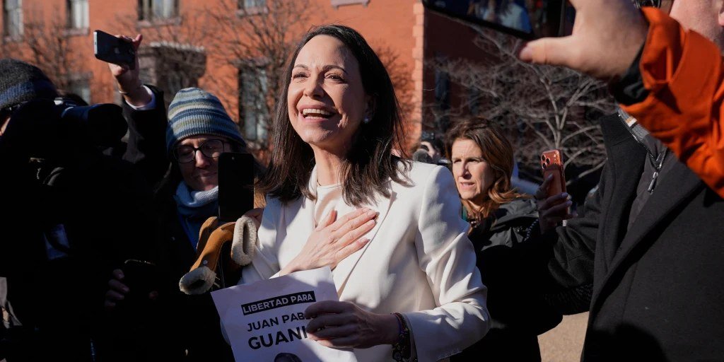 María Corina Machado sonríe con la mano en el pecho rodeada de personas que la graban con sus teléfonos al aire libre.