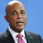 Michel Martelly habla con traje oscuro y corbata rosada ante un fondo azul