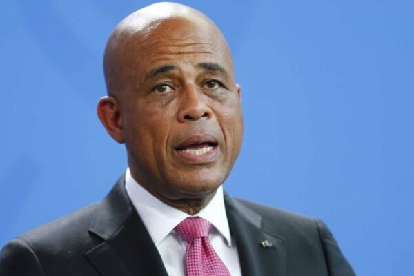 Michel Martelly habla con traje oscuro y corbata rosada ante un fondo azul