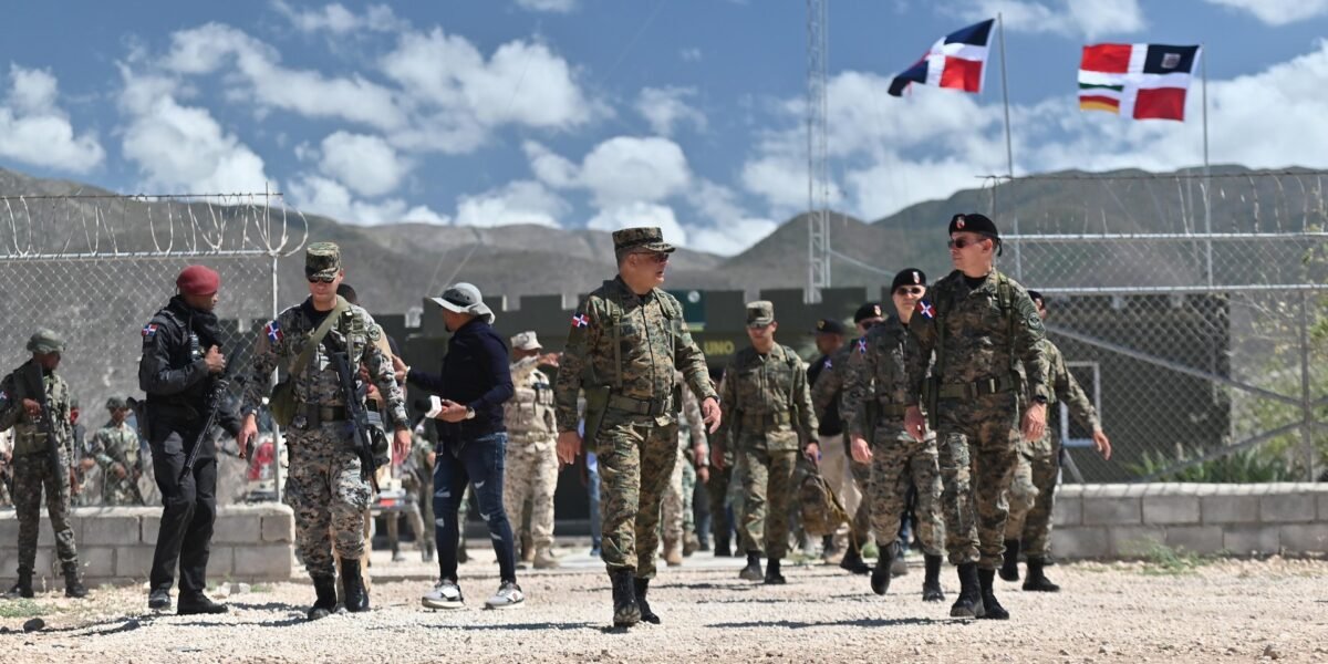 Militares dominicanos caminan en un puesto fronterizo con alambrada y banderas dominicanas al fondo