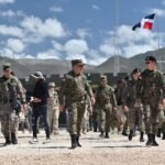Militares dominicanos caminan en un puesto fronterizo con alambrada y banderas dominicanas al fondo