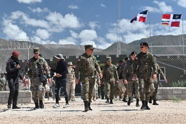 Militares dominicanos caminan en un puesto fronterizo con alambrada y banderas dominicanas al fondo