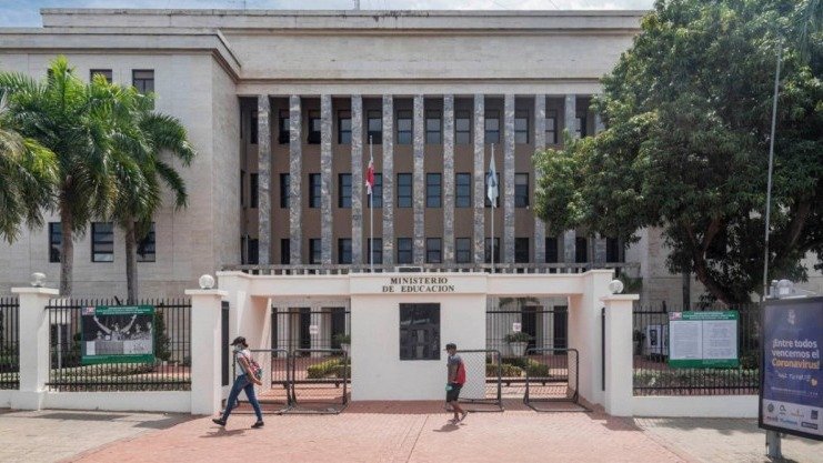 Fachada de la sede del Ministerio de Educación, con columnas, banderas, palmeras y la entrada con el letrero del ministerio