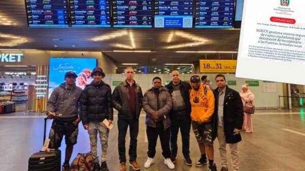 Siete hombres posan con maletas en la terminal de un aeropuerto, bajo pantallas de vuelos; a la derecha, la imagen de un comunicado del Ministerio de Relaciones Exteriores