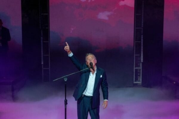 Ricardo Montaner canta en un escenario con luces violetas y humo, con el brazo en alto
