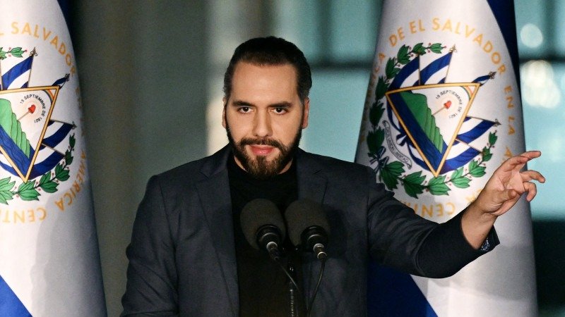 Nayib Bukele habla ante dos micrófonos en un atril, con banderas de El Salvador a ambos lados