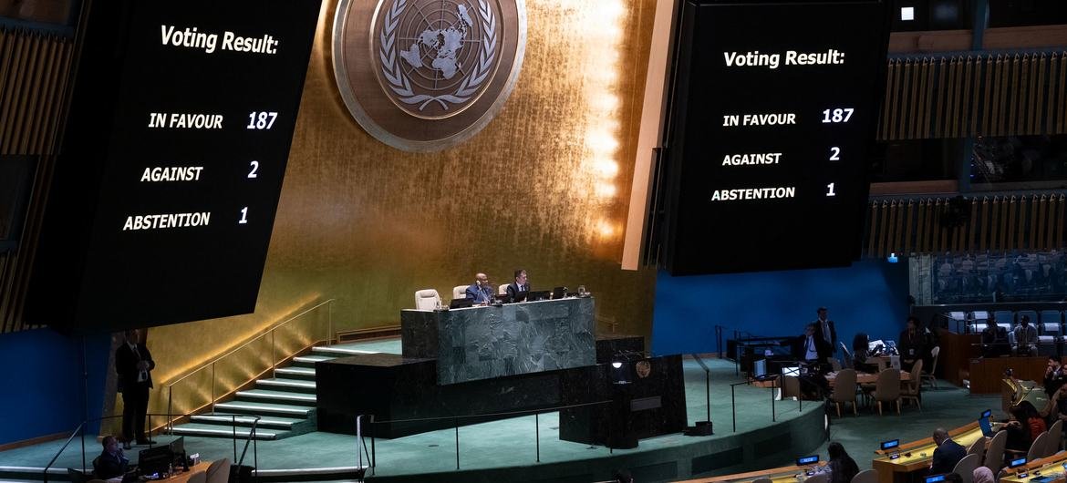 Salón de la Asamblea General de la ONU con el emblema dorado al fondo y dos pantallas que muestran el resultado de una votación anterior