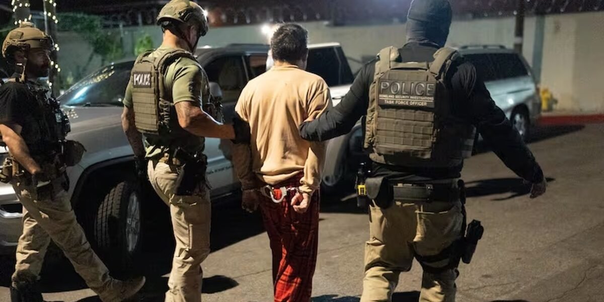 Agentes federales con chalecos escoltan de noche a un hombre esposado, de espaldas, hacia un vehículo