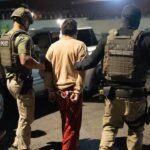 Agentes federales con chalecos escoltan de noche a un hombre esposado, de espaldas, hacia un vehículo