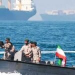 Militares iraníes en una lancha armada con bandera de Irán navegan frente a buques mercantes
