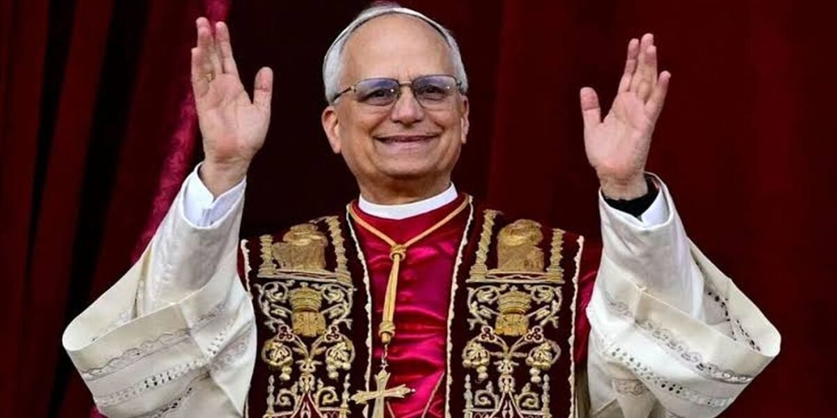 El papa León XIV, con estola bordada y muceta roja, saluda con ambos brazos en alto ante una cortina roja