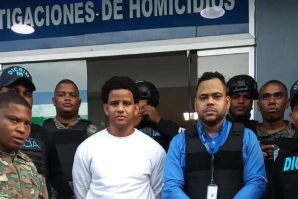 Bryan Rafael Gómez, de ropa blanca, custodiado por agentes de la DICRIM, militares y un representante del Ministerio Público frente al letrero de Investigaciones de Homicidios