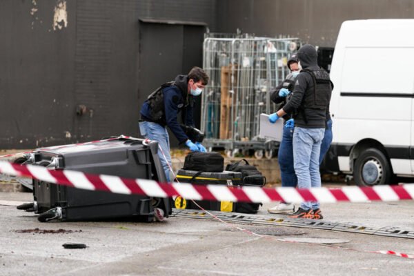 Agentes de la policía francesa con guantes y mascarilla recogen pruebas detrás de una cinta de acordonamiento roja y blanca