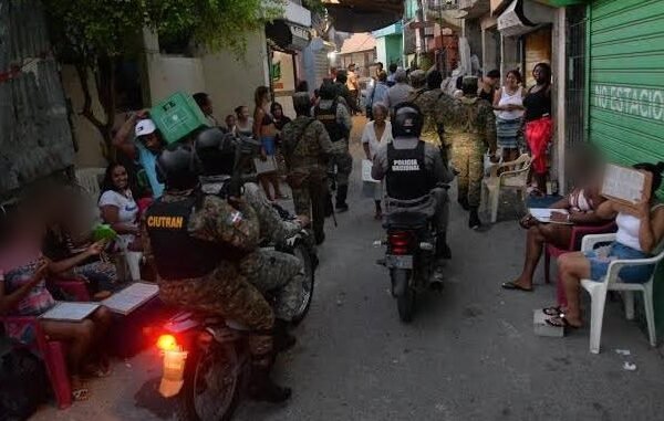Agentes de la Policía Nacional y militares en motocicleta y a pie recorren un callejón estrecho mientras vecinos observan sentados frente a sus casas