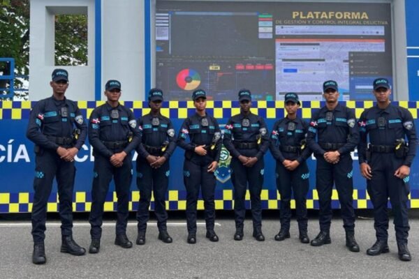 Agentes de la Policía Nacional en uniforme azul posan en fila frente a una estación policial móvil.