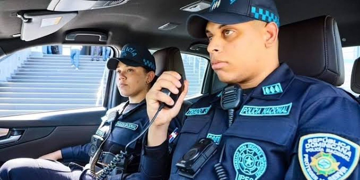 Dos agentes de la Policía Nacional dentro de una patrulla; uno habla por radio.