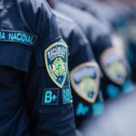 Policía apresa a dos por robo de RD$1.4 millones en joyería de Santiago Detalle de la manga del uniforme de la Policía Nacional con el escudo institucional, con agentes en fila al fondo.
