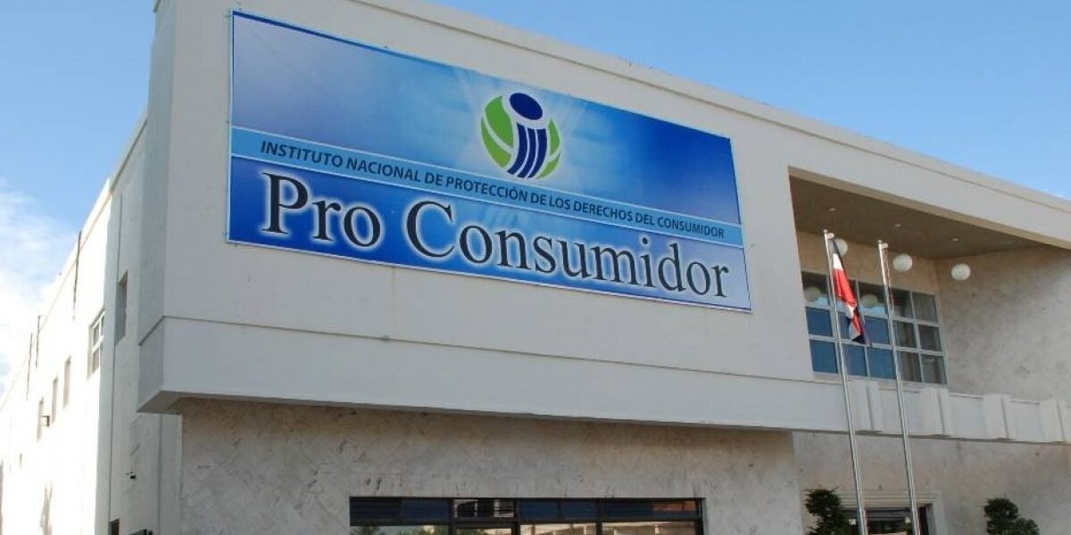 Fachada de un edificio blanco con un letrero azul del Instituto Nacional de Protección de los Derechos del Consumidor, Pro Consumidor, y una bandera dominicana