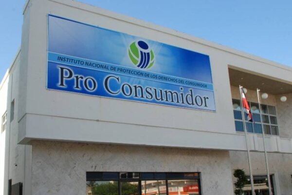 Fachada de un edificio blanco con un letrero azul del Instituto Nacional de Protección de los Derechos del Consumidor, Pro Consumidor, y una bandera dominicana