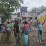 La Vega: vecinos de El Tanque Arriba protestan para exigir el asfaltado de su calle Vecinos con carteles de papel en una calle de tierra con piedras, casas y motocicletas al fondo