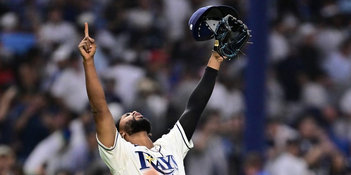 Un jugador de los Rays de Tampa Bay celebra con los brazos en alto, la gorra y el guante en una mano