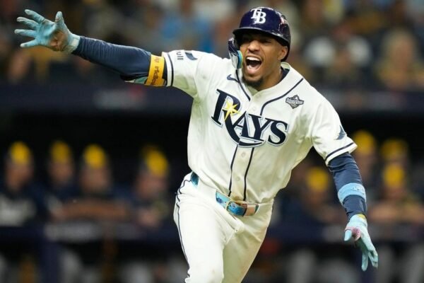 Un jugador de los Rays de Tampa Bay, con casco y uniforme blanco con el parche de la Serie Mundial, celebra con los brazos abiertos.