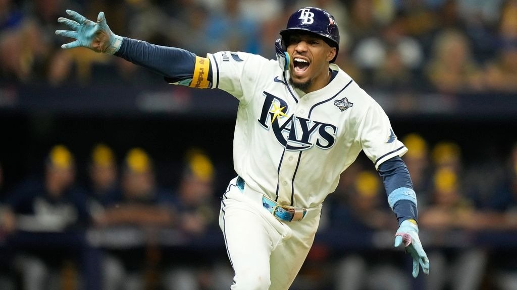 Un jugador de los Rays de Tampa Bay, con casco y uniforme blanco con el parche de la Serie Mundial, celebra con los brazos abiertos.