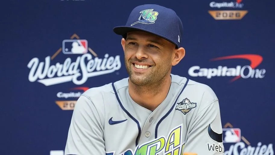 Un jugador con gorra y uniforme gris de los Rays de Tampa Bay sonríe durante una conferencia de prensa ante un fondo de la Serie Mundial 2026.
