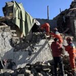 Bomberos con uniforme naranja trabajan sobre los escombros de una vivienda de piedra derrumbada, foto de archivo