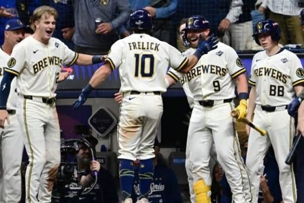 El jugador número 10 de los Cerveceros, Frelick, de espaldas, es recibido por sus compañeros con uniforme blanco frente al dugout