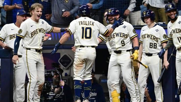 El jugador número 10 de los Cerveceros, Frelick, de espaldas, es recibido por sus compañeros con uniforme blanco frente al dugout