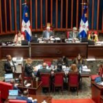 Senadores y personal técnico durante una sesión en el hemiciclo del Senado dominicano, con la mesa directiva y dos banderas dominicanas al fondo