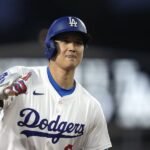 Shohei Ohtani con casco y uniforme de los Dodgers, señalando con la mano mientras corre en el terreno.