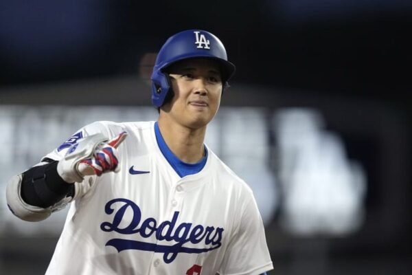 Shohei Ohtani con casco y uniforme de los Dodgers, señalando con la mano mientras corre en el terreno.