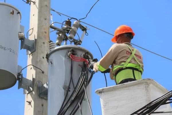 Un técnico con casco naranja y chaleco reflectante trabaja desde una canasta elevada en los transformadores de un poste eléctrico