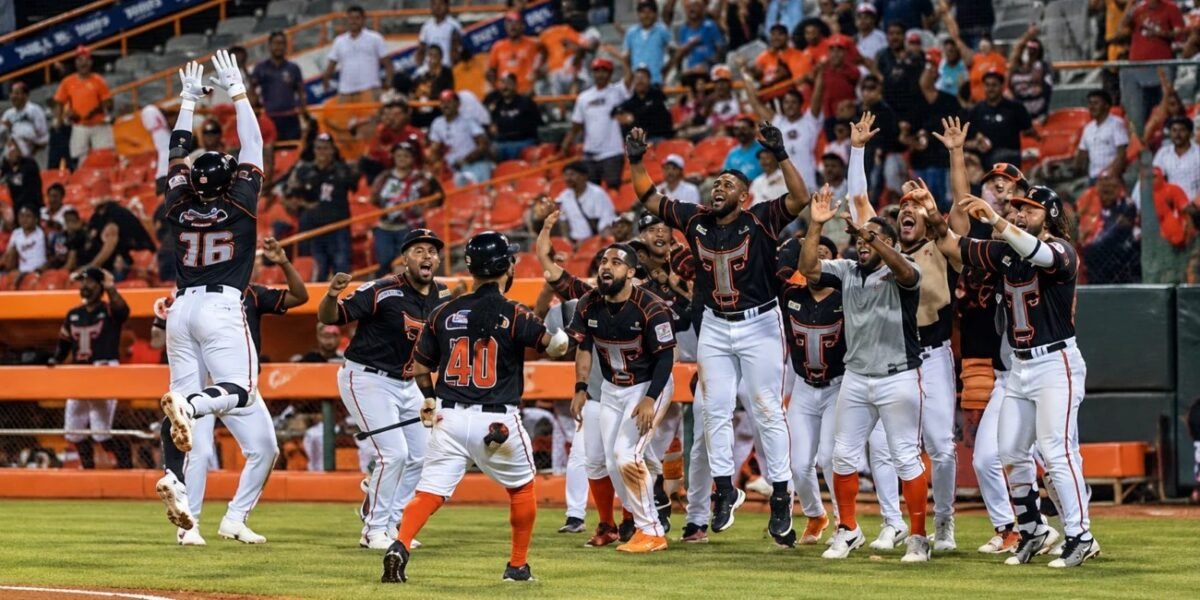 Jugadores de los Toros del Este, con uniforme negro, blanco y anaranjado, celebran con los brazos en alto frente al dugout mientras el público aplaude en las gradas