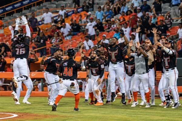Jugadores de los Toros del Este, con uniforme negro, blanco y anaranjado, celebran con los brazos en alto frente al dugout mientras el público aplaude en las gradas