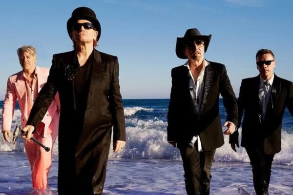 Los cuatro integrantes de U2 caminan por la orilla del mar vestidos de traje, en una imagen promocional