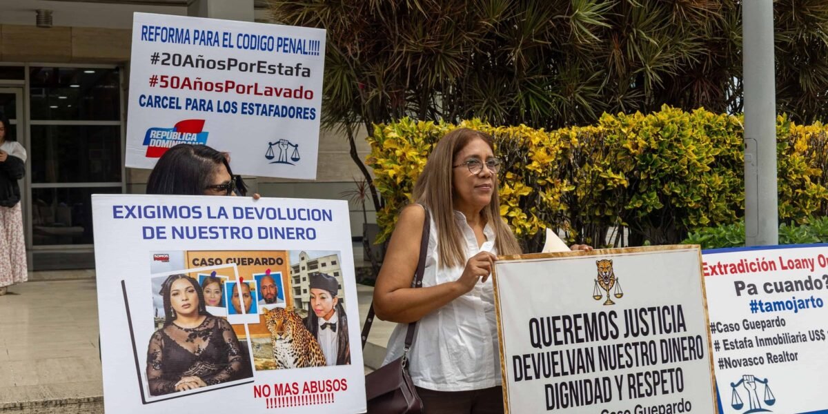 Dos mujeres sostienen pancartas que piden justicia y la devolución de su dinero, firmadas por las víctimas del caso Guepardo, frente a un edificio.
