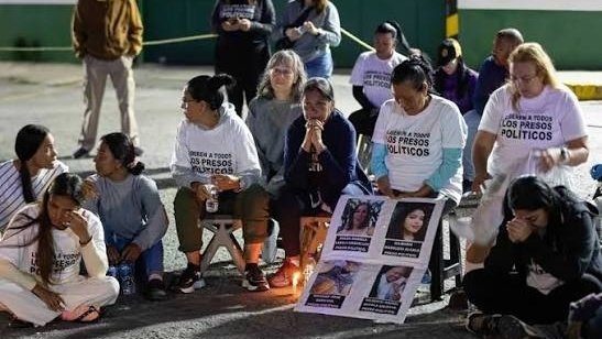 Mujeres con camisetas que piden liberar a los presos políticos, sentadas de noche junto a velas y carteles con fotos de detenidos.